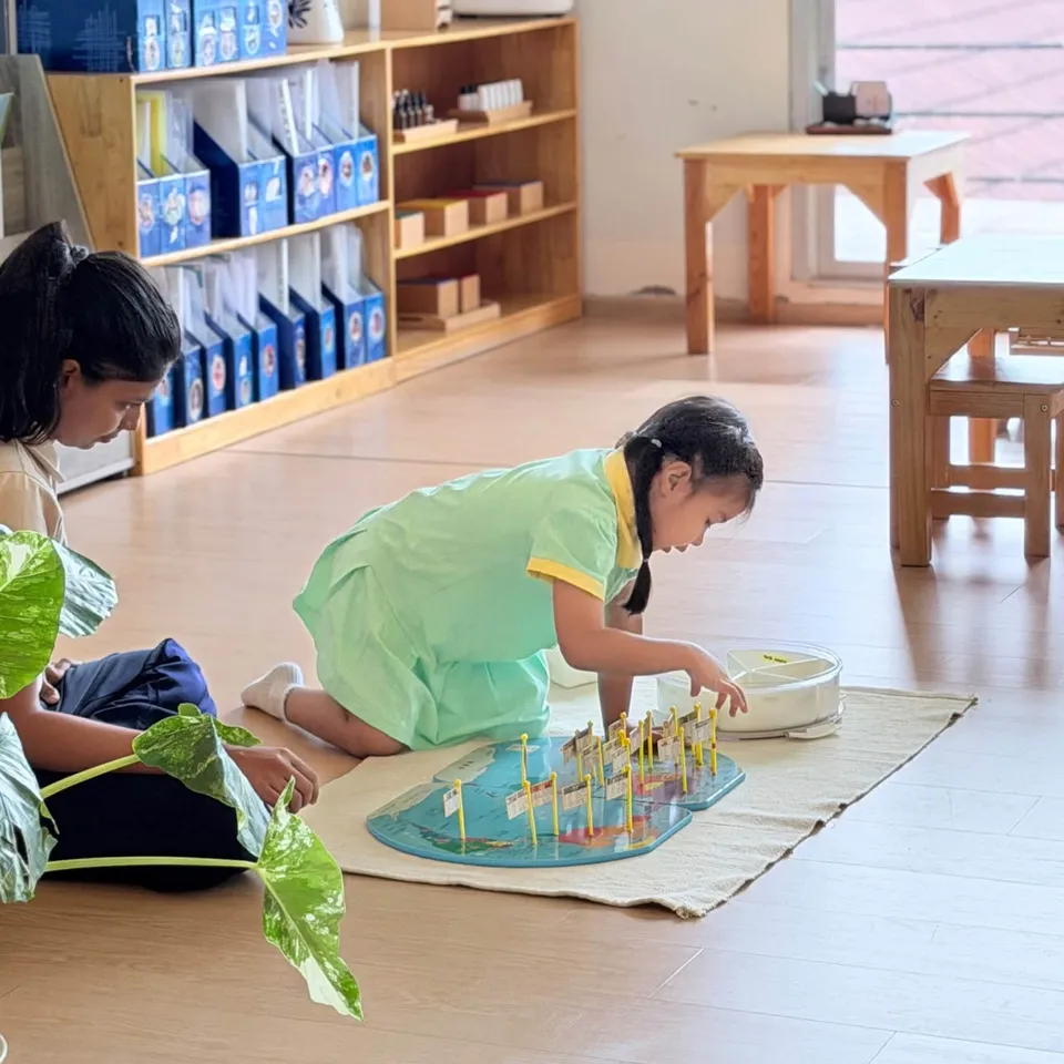 A girl kneels on a mat placing small flags on a world map puzzle