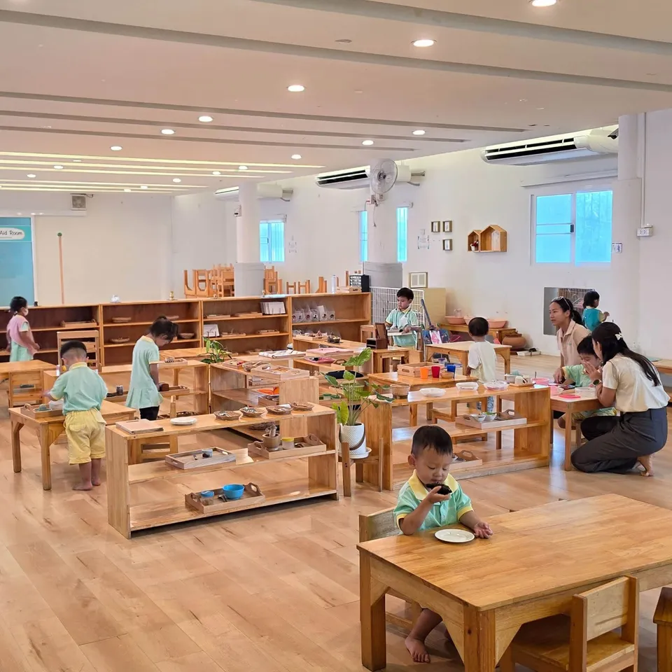 Toddlers choosing work from low shelves while teachers kneel at their level