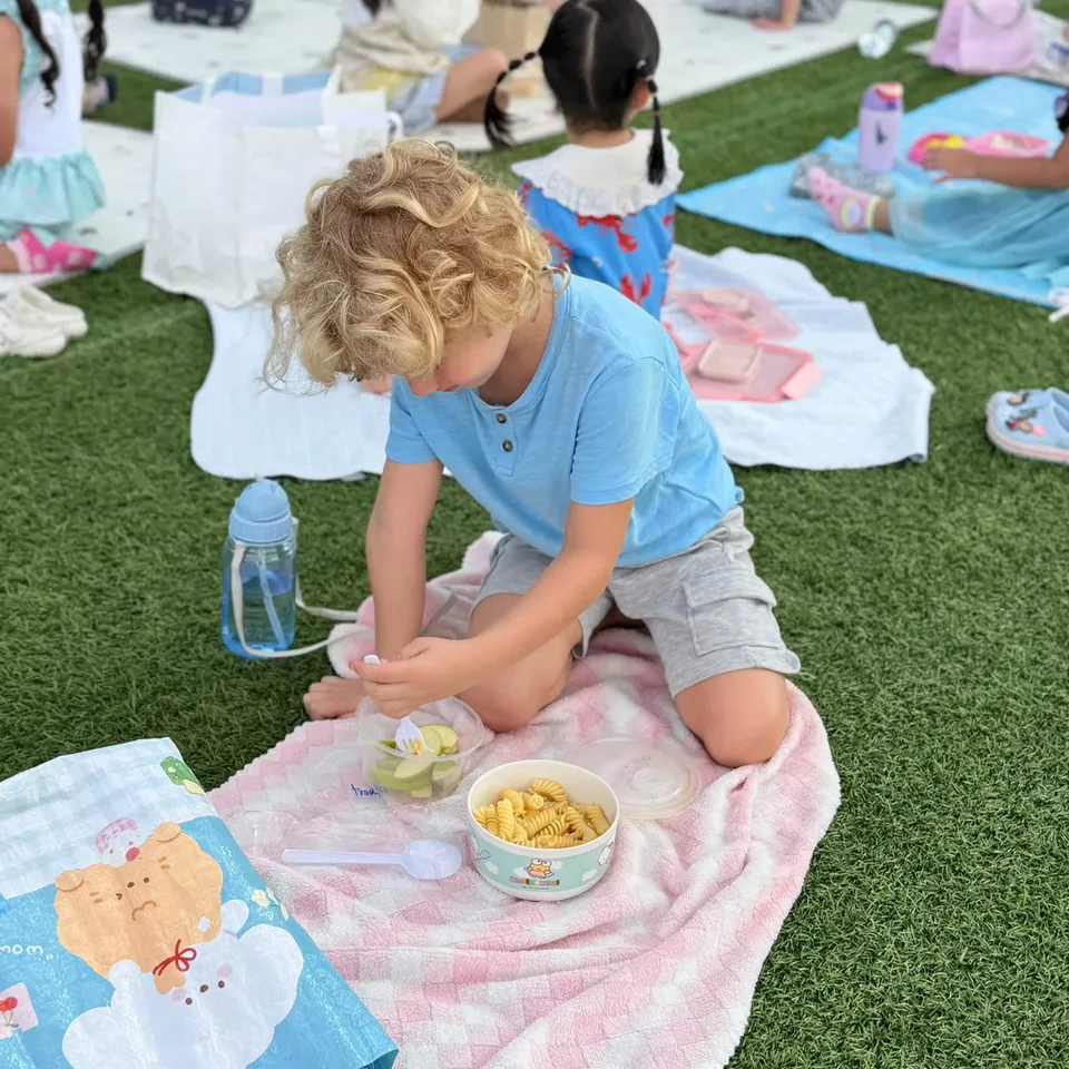 A boy kneeling on a picnic blanket eating apple slices and pasta